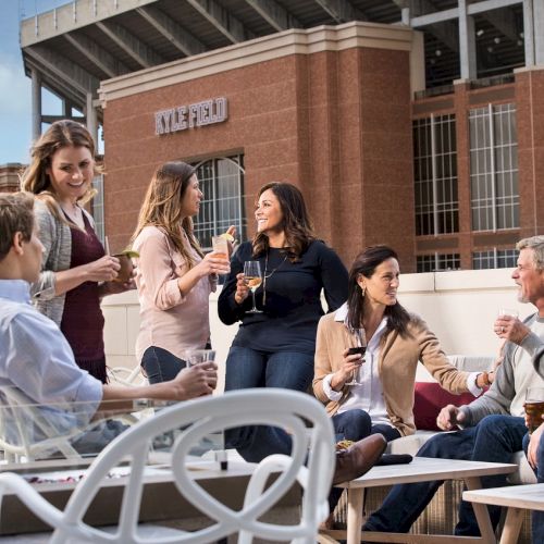 Guests enjoying drinks and conversation around outdoor seating on 2nd floor balcony overlooking Kyle Field