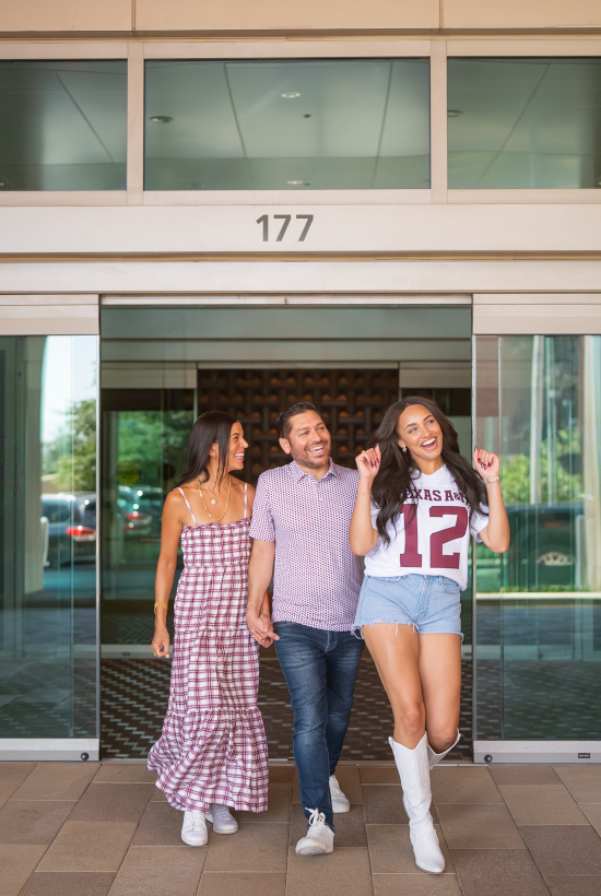 Three friends stroll out of office entrance 177, smiling and waving under glass doors, with palm plants beside them.