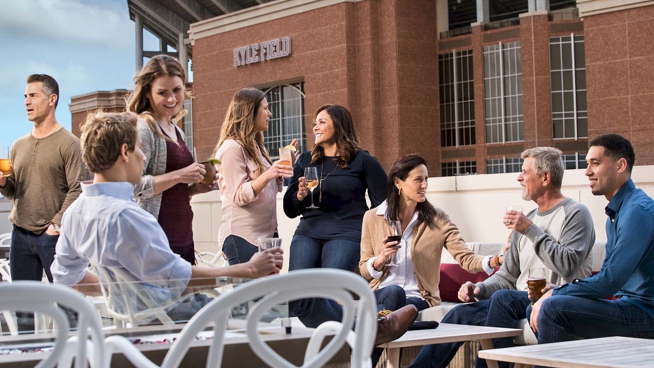 Men and women enjoying drinks and conversation on the Block T balcony overlooking Kyle Field