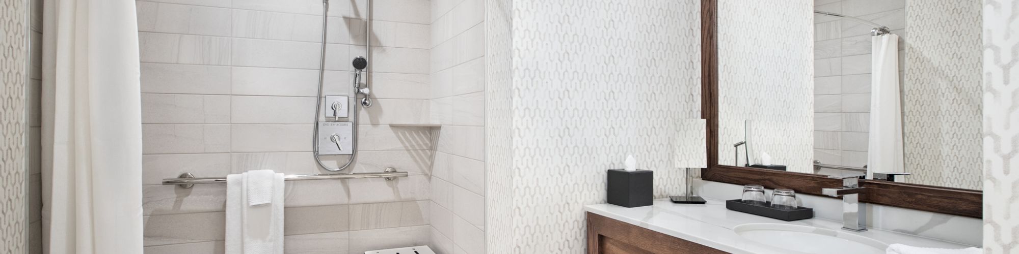 A modern accessible bathroom with a walk-in shower, built-in bench, and a white vanity with mirror and towels.
