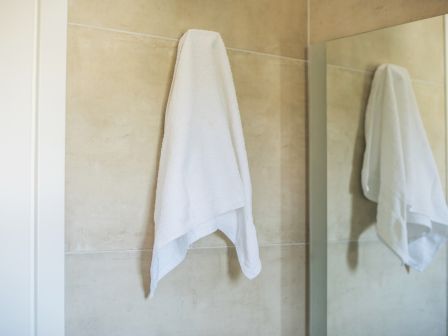 A white towel hanging on a bathroom wall, its reflection visible in a mirror.