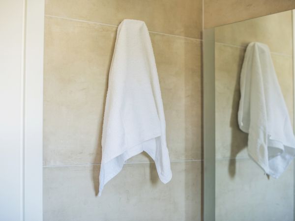 A white towel hanging on a bathroom wall, its reflection visible in a mirror.