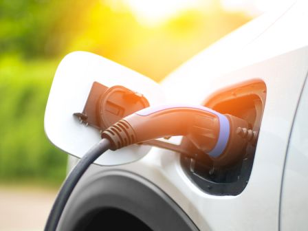 An electric vehicle charging&mdash;an orange plug and cable connected to the car in sunny outdoor light.