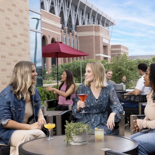 Group of friends relaxing at an outdoor cafe on a sunny day, chatting and sipping colorful drinks on a modern patio.