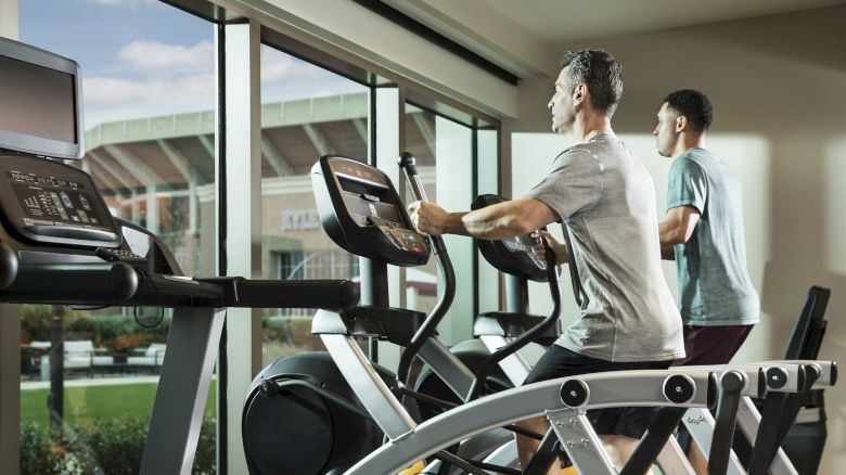 Two men running on elliptical machines in the gym overlooking Kyle Field