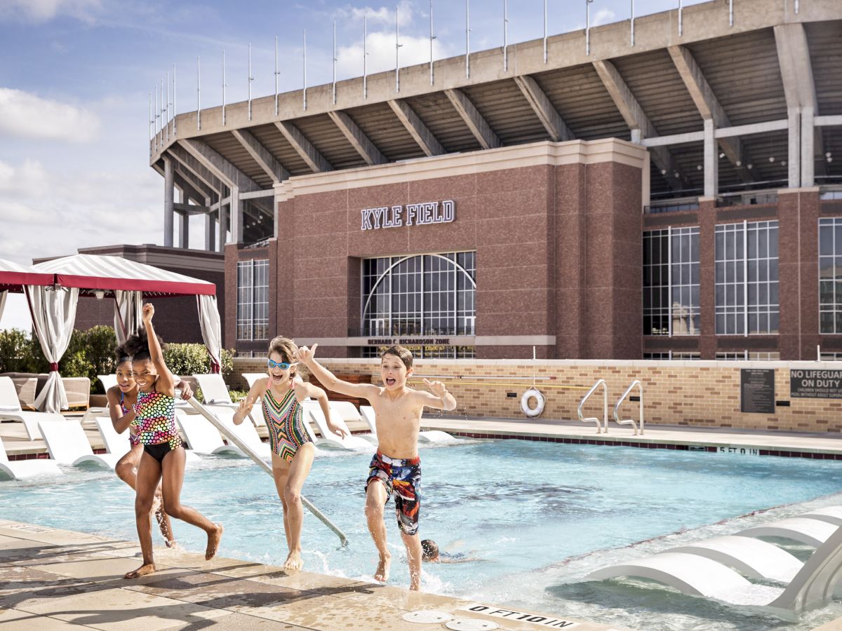 Kids running up the stairs of the rooftop pool with a view of Kyle Field in the background