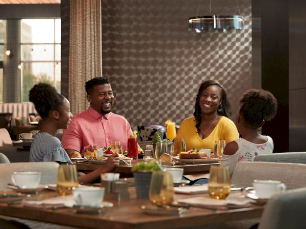 A group of people enjoy a meal at a restaurant table, smiling and chatting as drinks and food sit before them.