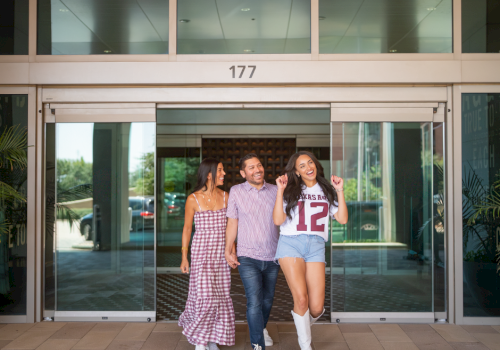 Three friends walk and smile outside a building entrance, with number 177 above the doors.