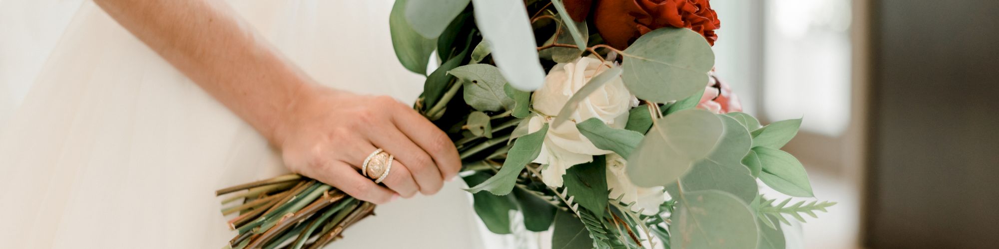 A person hands over a bouquet of roses and eucalyptus leaves in white, red, and pink tones.