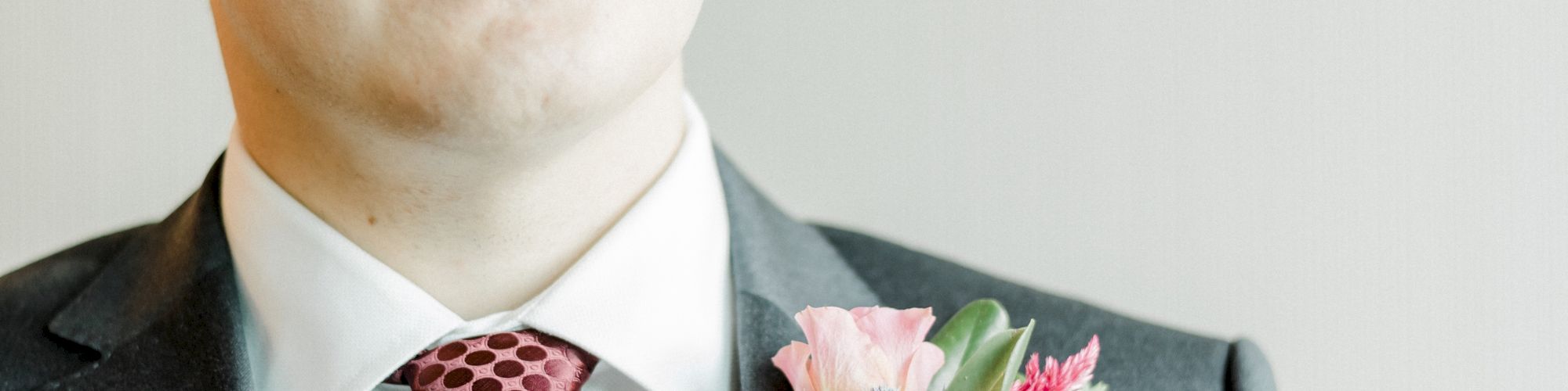 A man in a dark suit with a patterned pink tie, wearing a floral boutonniere in a studio portrait.