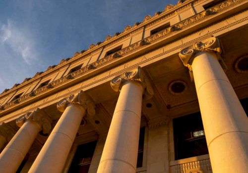 A grand neoclassical building fa&ccedil;ade with ornate gold trim and tall white columns under a blue sky.