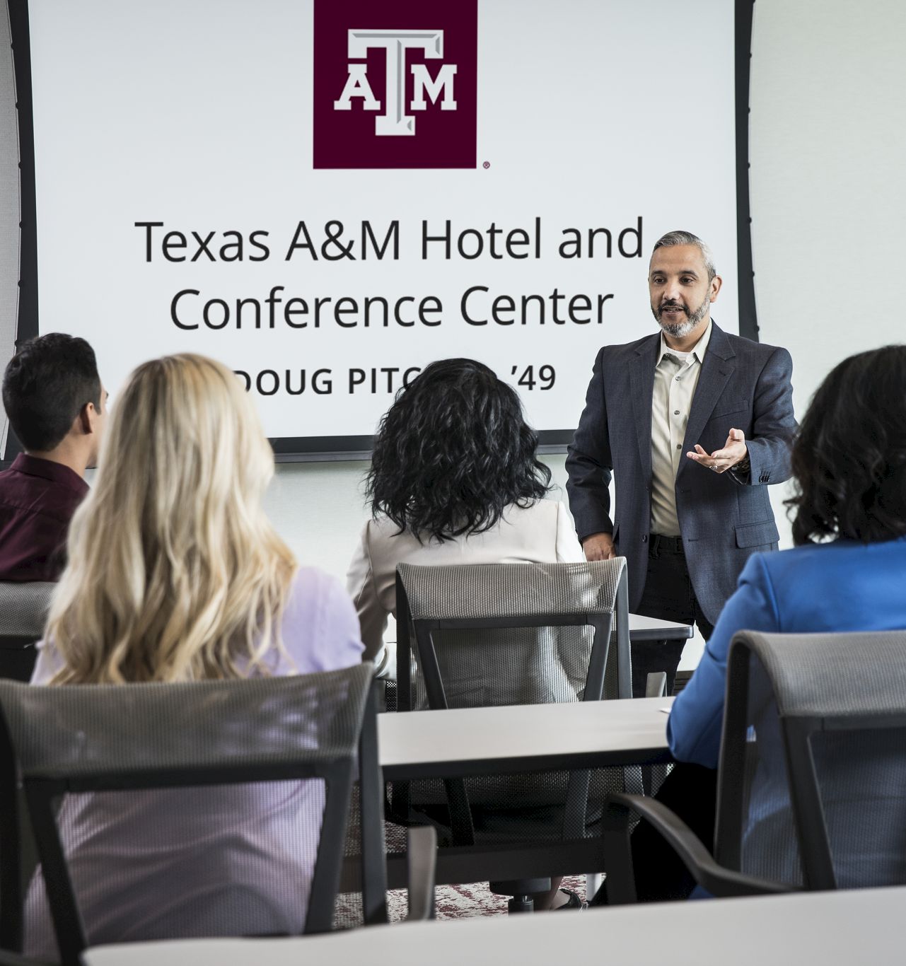 A speaker addresses attendees in a conference room at the Texas A&M Hotel and Conference Center during a presentation.