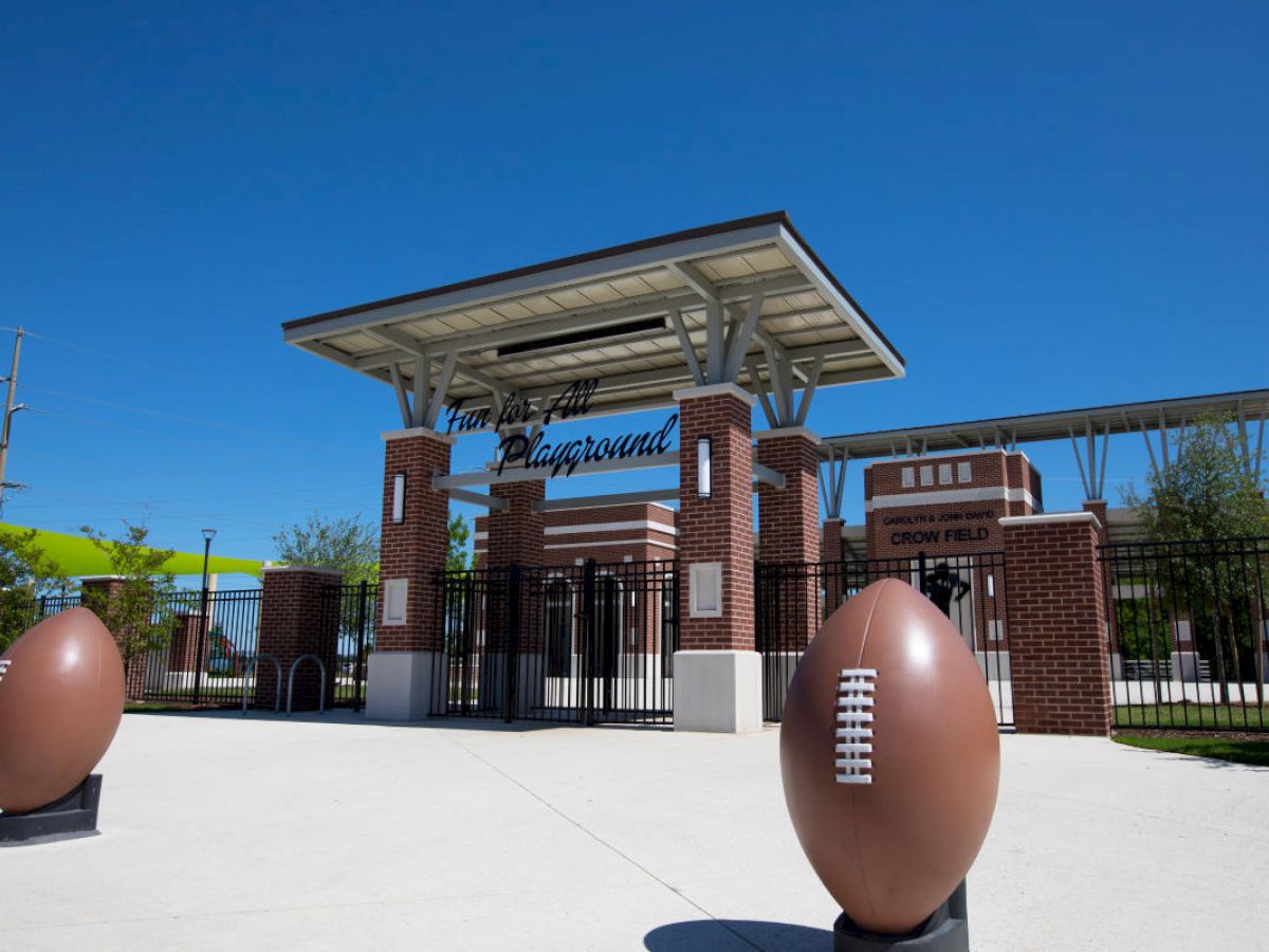 The image shows the entrance to a sports playground named "Crown Field." There are two large football sculptures flanking the path.