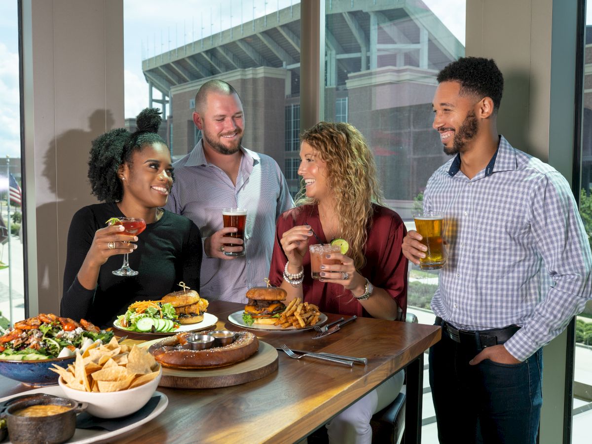 Four people are standing around a table with food and drinks, smiling and enjoying their time together.
