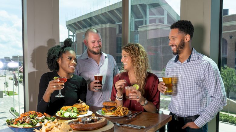 Four people are standing around a table with food and drinks, smiling and enjoying their time together.