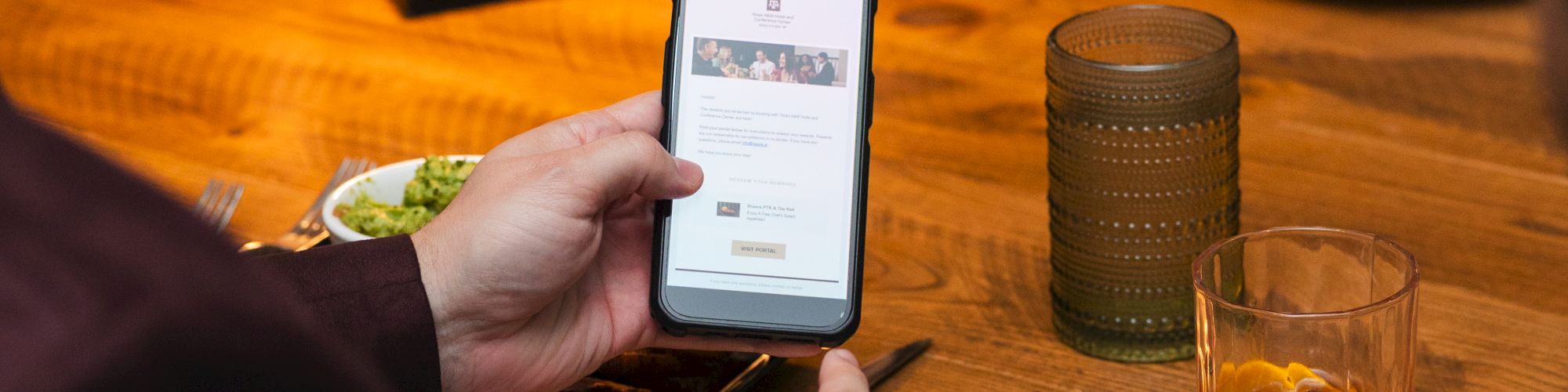 A person at a restaurant holds a smartphone, seemingly checking a menu or ticket, while drinks and food sit on the table.