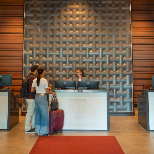 People chat at a reception desk with a Texas A&M logo backdrop inside an office lobby.