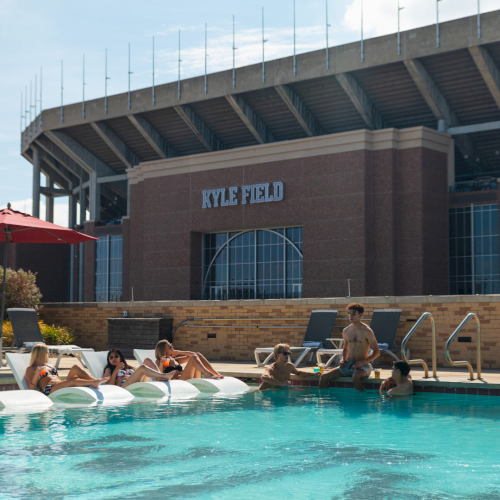 People swim in a pool in front of Kyle Field stadium, where &ldquo;KYLE FIELD&rdquo; is displayed.