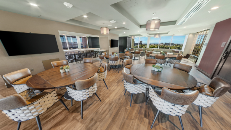 A modern conference room with wooden tables, woven chairs, pendant lights, TV screens, and large windows overlooking the outdoors.