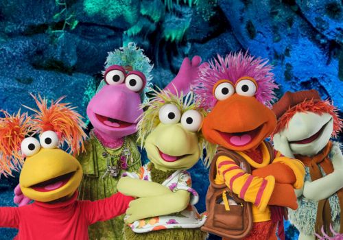 Five colorful Sesame Street-style puppet characters sing together in an underwater blue cave, wearing bright wigs and costumes.