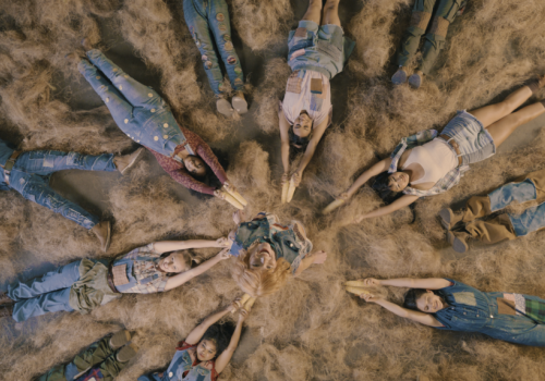 Top-down: people in denim and plaid lie together on dry grass, smiling in a circle.