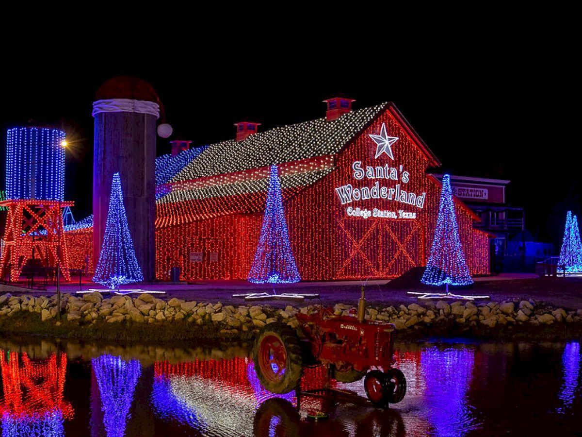 A festive barn is decorated with colorful Christmas lights and a sign that reads "Santa's Wonderland, College Station, Texas."
