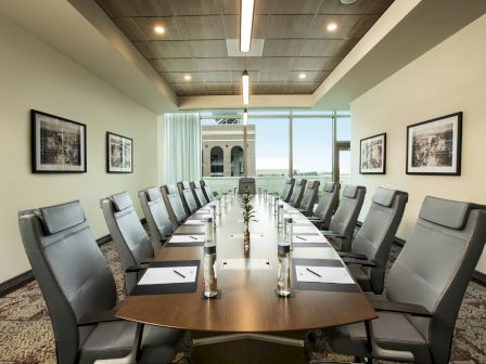 A modern conference room with a long table, twelve chairs, notepads, and water bottles arranged neatly. Art pieces hang on the walls.