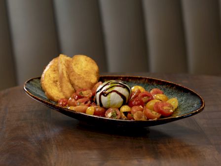A plate with sliced tomatoes, a ball of cheese drizzled with balsamic glaze, and crispy bread.