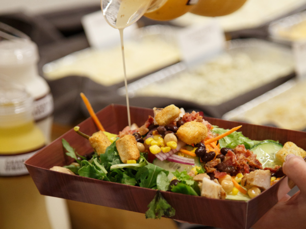 Someone pouring dressing over a salad at the gameday salad bar