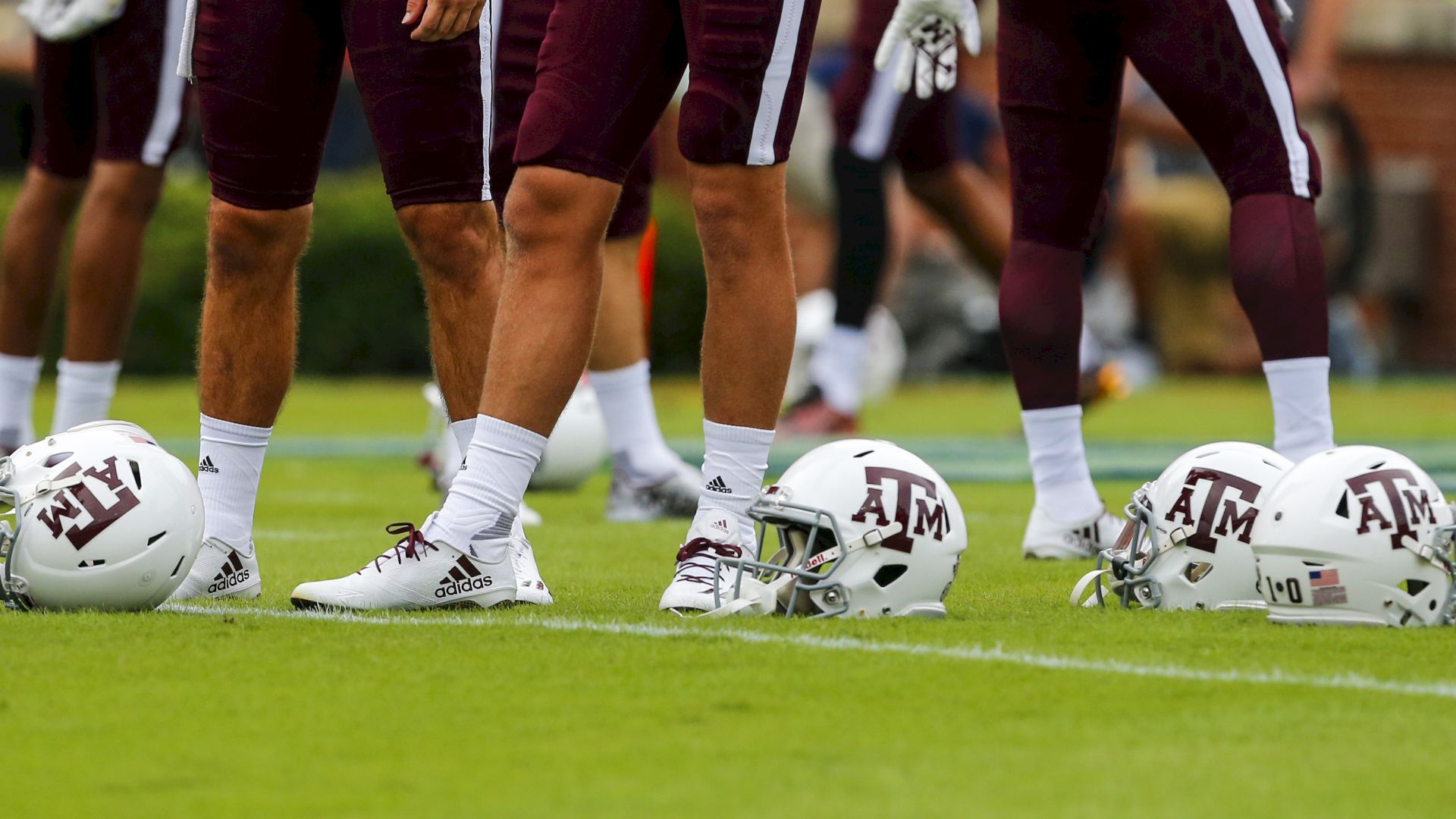 Football players standing on a field with their white helmets on the ground, marked with "A&M" logos on them.