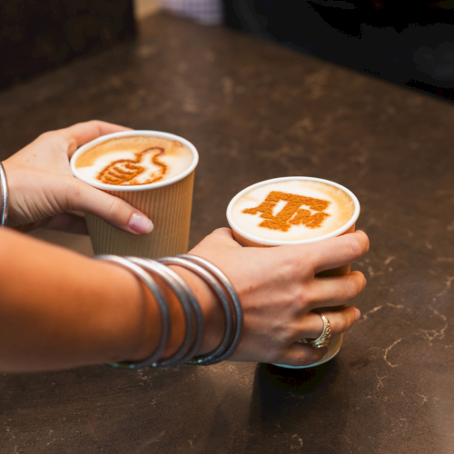 Two hands clink paper cups of latte with cinnamon latte art, enjoying a warm coffee moment together.