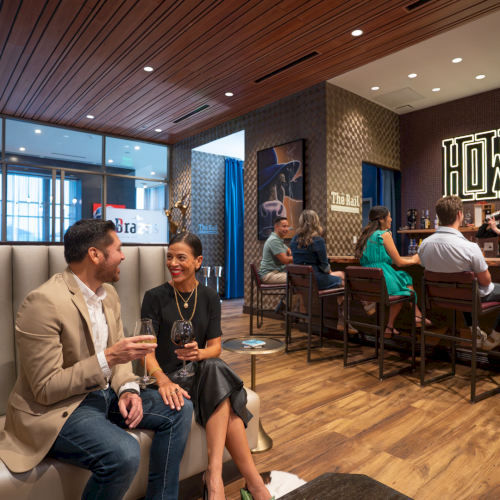 A stylish lounge/bar area where friends chat and enjoy drinks, with &ldquo;The Rail&rdquo; signage on the wall.