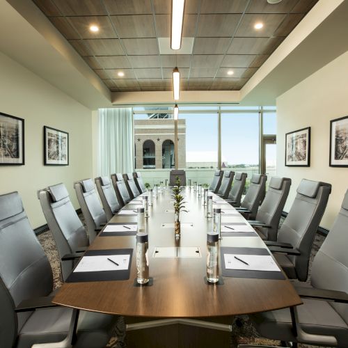 A well-lit conference room with a long table, leather chairs, water bottles, notepads, and wall art, facing a large window.