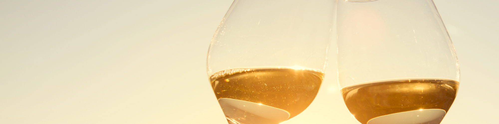 Two stemmed glasses of golden sparkling wine clink together under warm light, capturing a celebratory toast vibe.