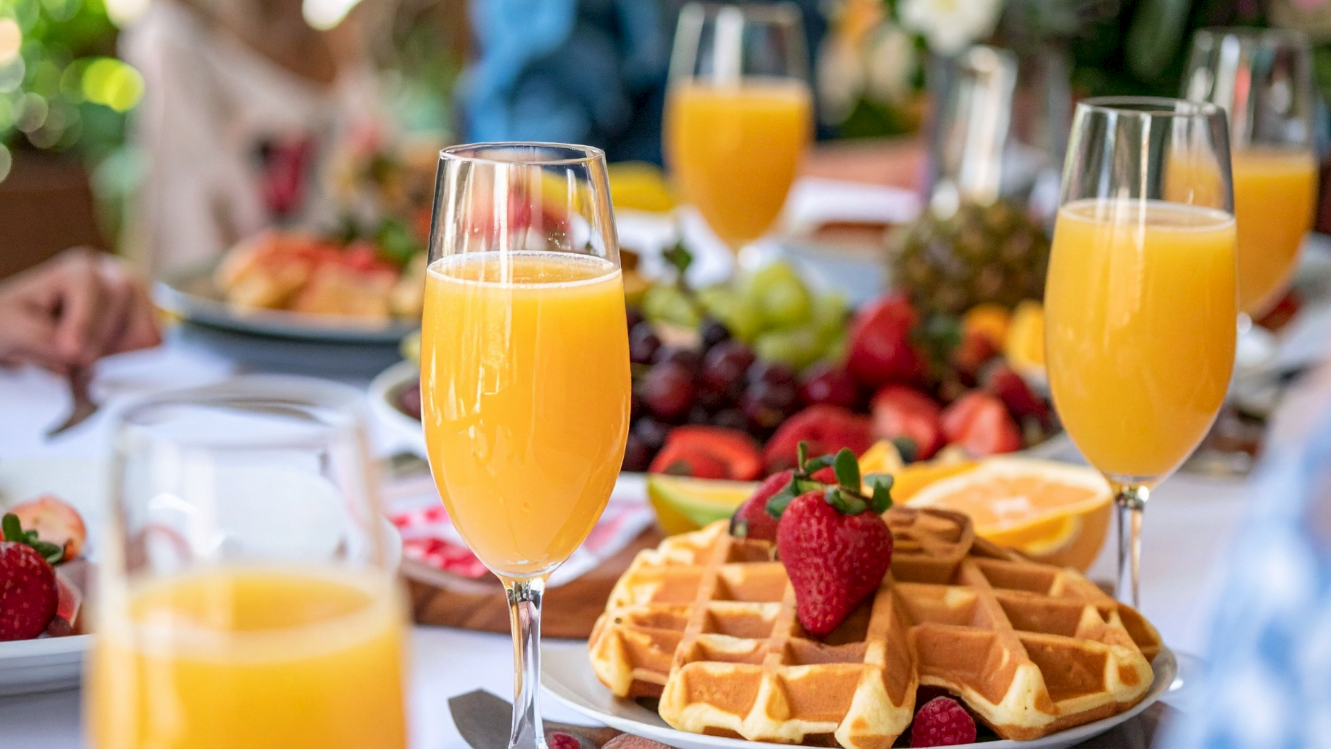 A bright table spread with waffles, strawberries, grapes, orange juice flutes, and fresh fruit for a sunny meal.