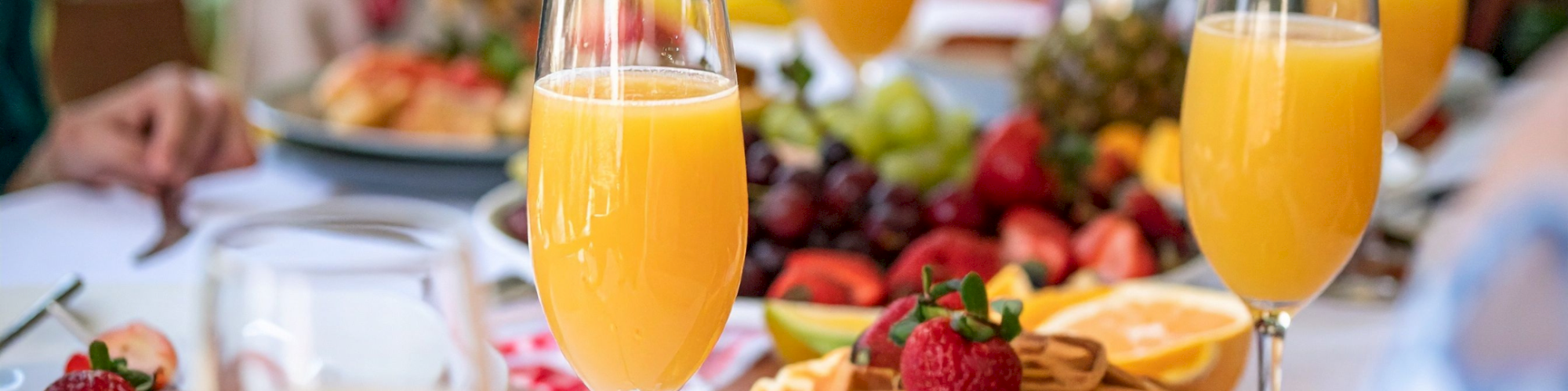 A bright table spread with waffles, strawberries, grapes, orange juice flutes, and fresh fruit for a sunny meal.