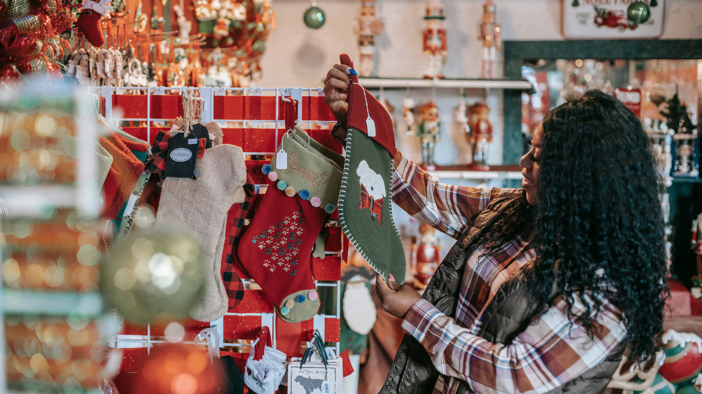 A person browses Christmas stockings in a festive store, surrounded by holiday decorations and ornaments.