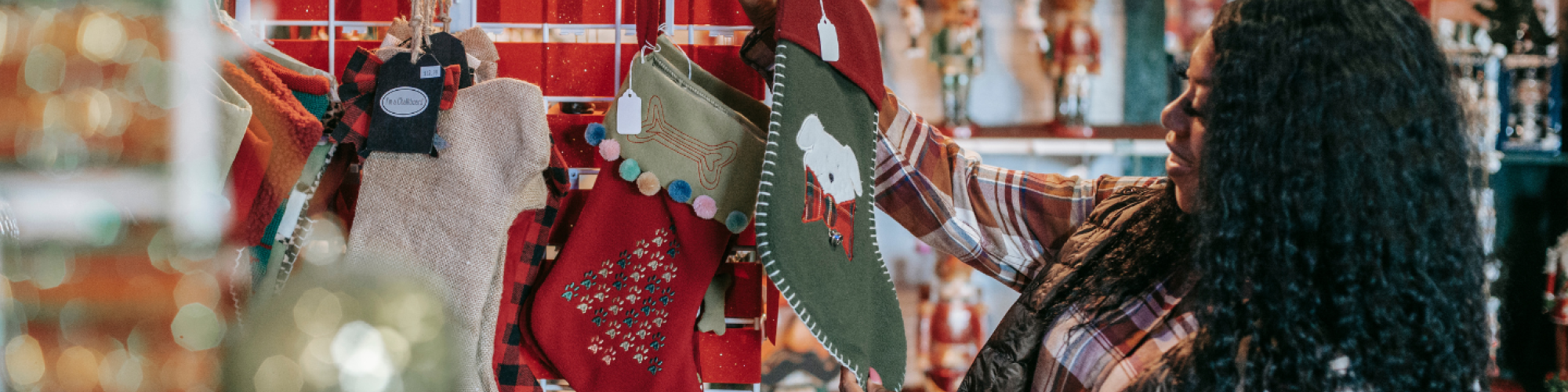 A person browses Christmas stockings in a festive store, surrounded by holiday decorations and ornaments.