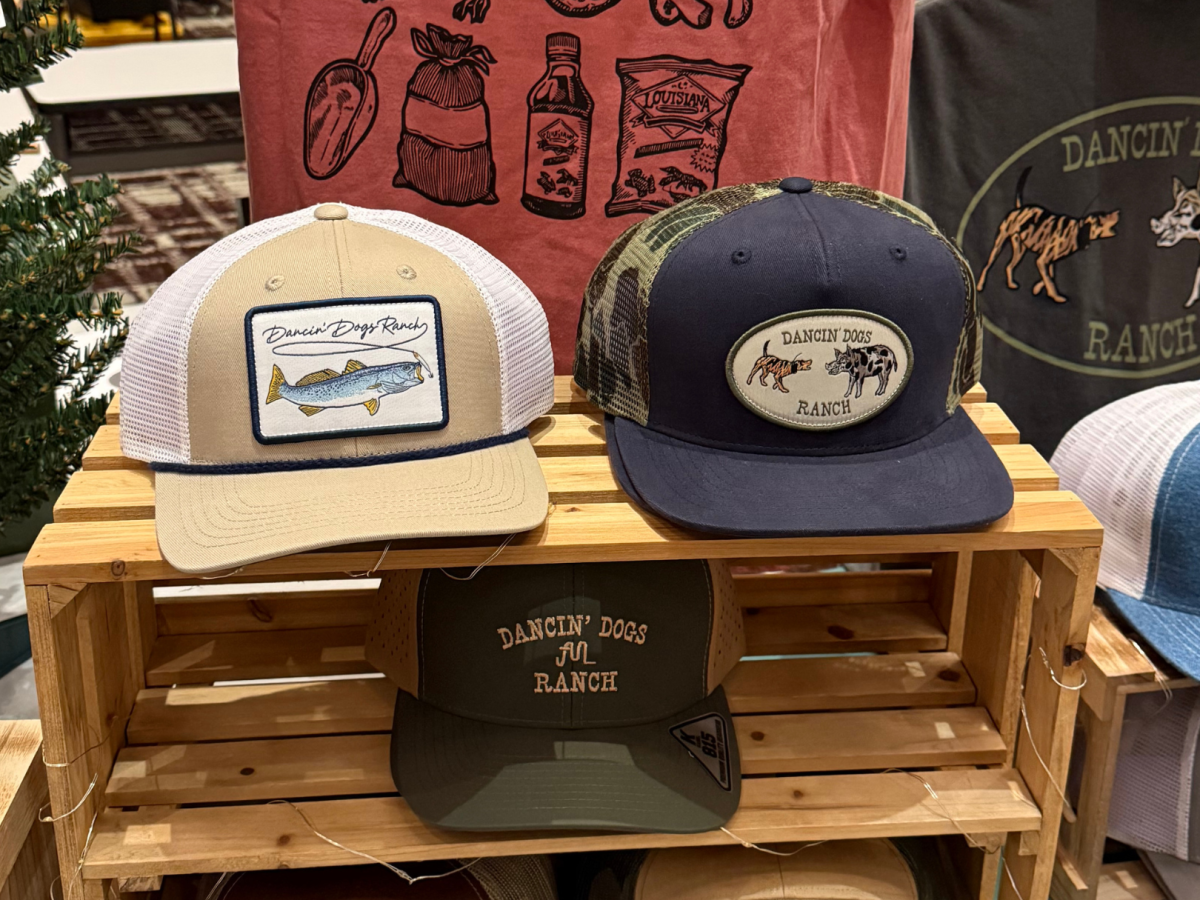 The image shows a display of five caps with various "Dancin' Dogs Ranch" designs and labels, arranged on a wooden shelf.